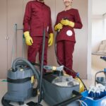 Cheerful housecleaners with cleaning equipment standing in room